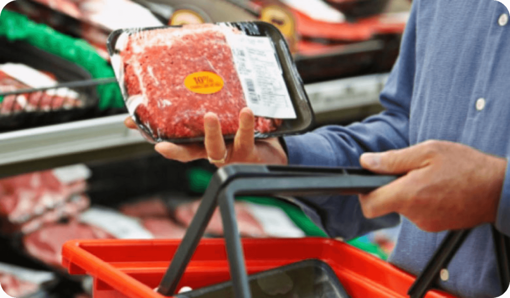 man holding package of beef in-store with handheld grocery cart